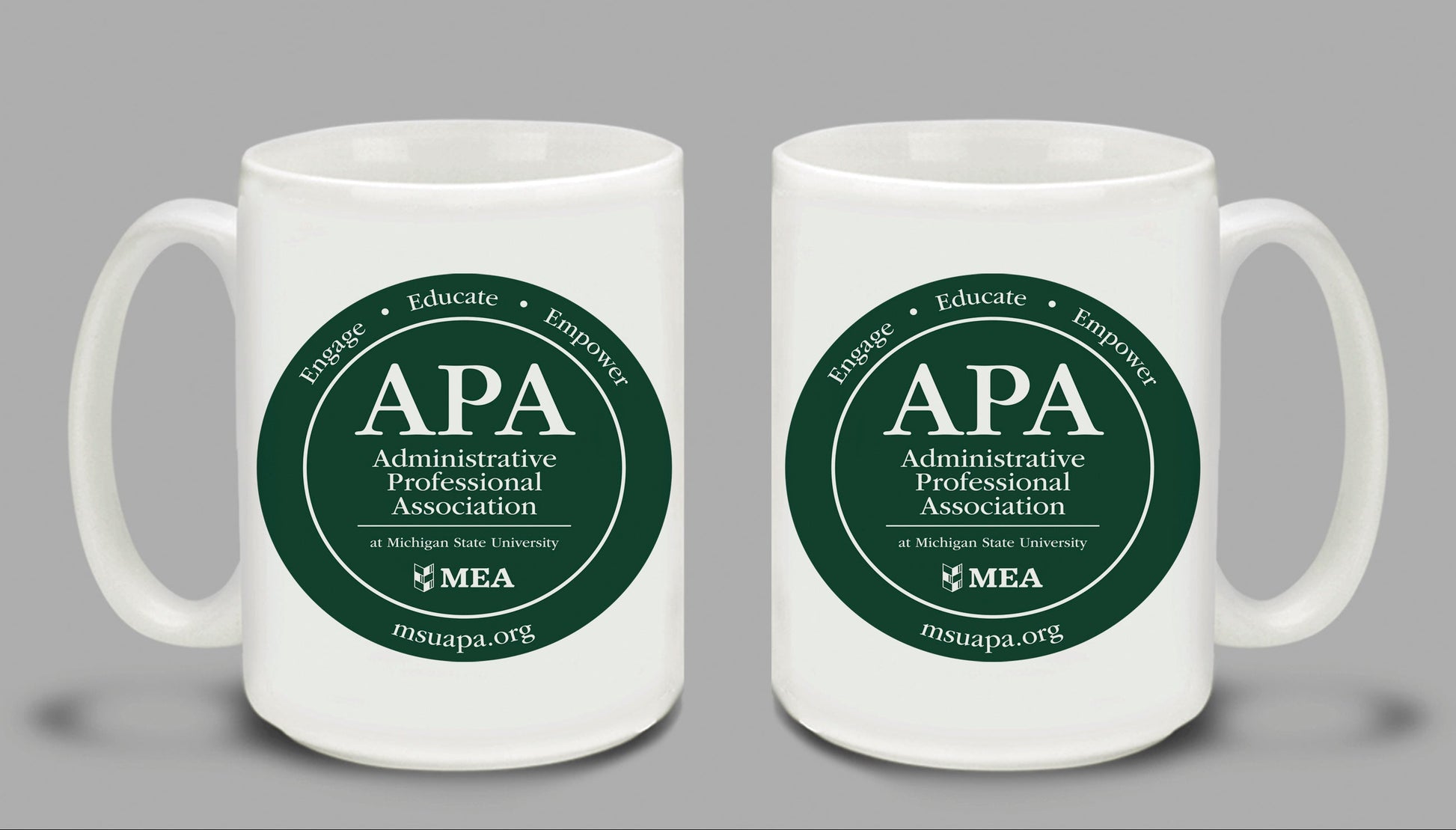 Two white mugs with green 'APA Administrative Professional Association' logos on a gray background.