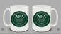 Two white mugs with green 'APA Administrative Professional Association' logos on a gray background.